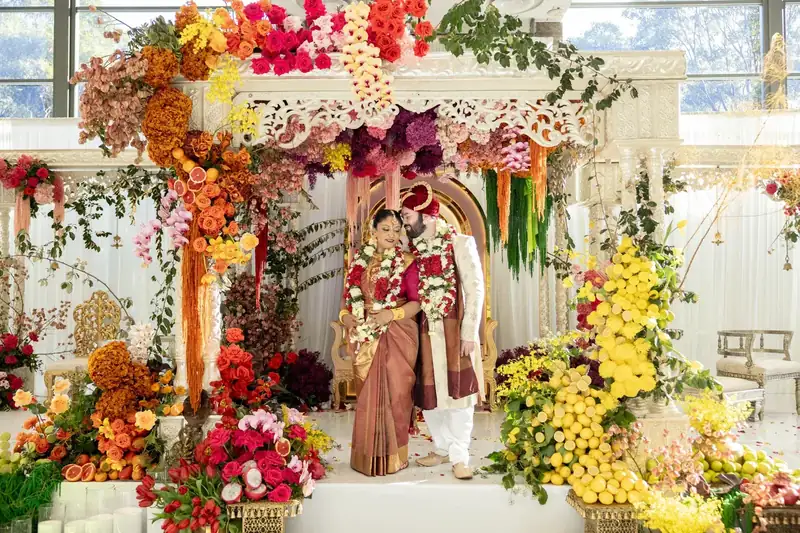 South Asian couple beneath a colorful floral wedding mandap